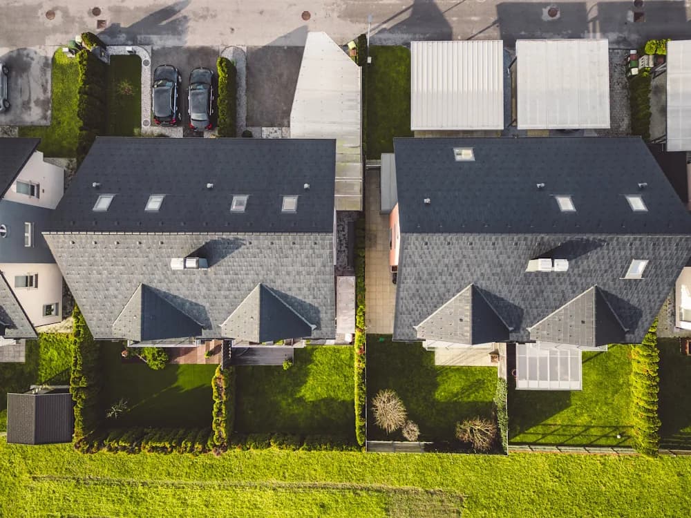 An overhead view of two adjoining duplex houses with shared rooflines and green lawns