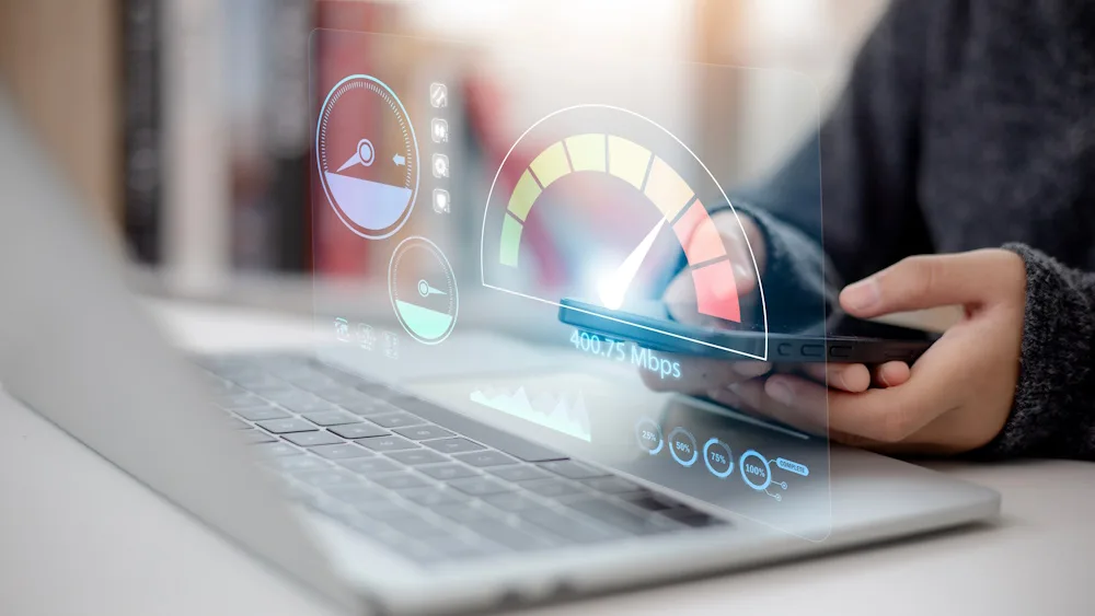 Hands hold a phone above a laptop showing a speed-test gauge reading 400.75 Mbps