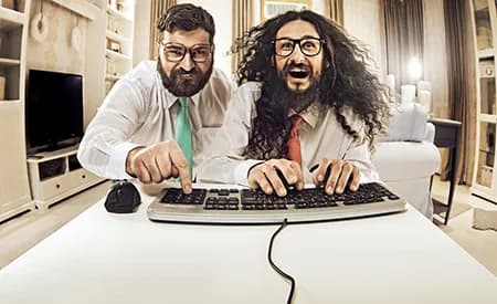 Two men in shirts and ties lean over a keyboard with exaggerated urgency