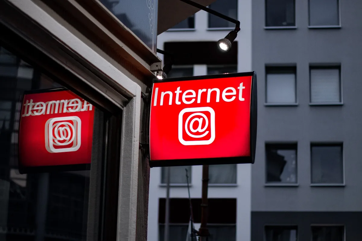 A red illuminated shop sign reading “Internet” with an @ symbol on a city street