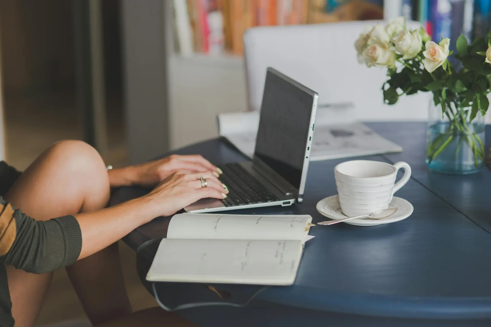 A person types on a laptop at a dark table with an open notebook and coffee cup