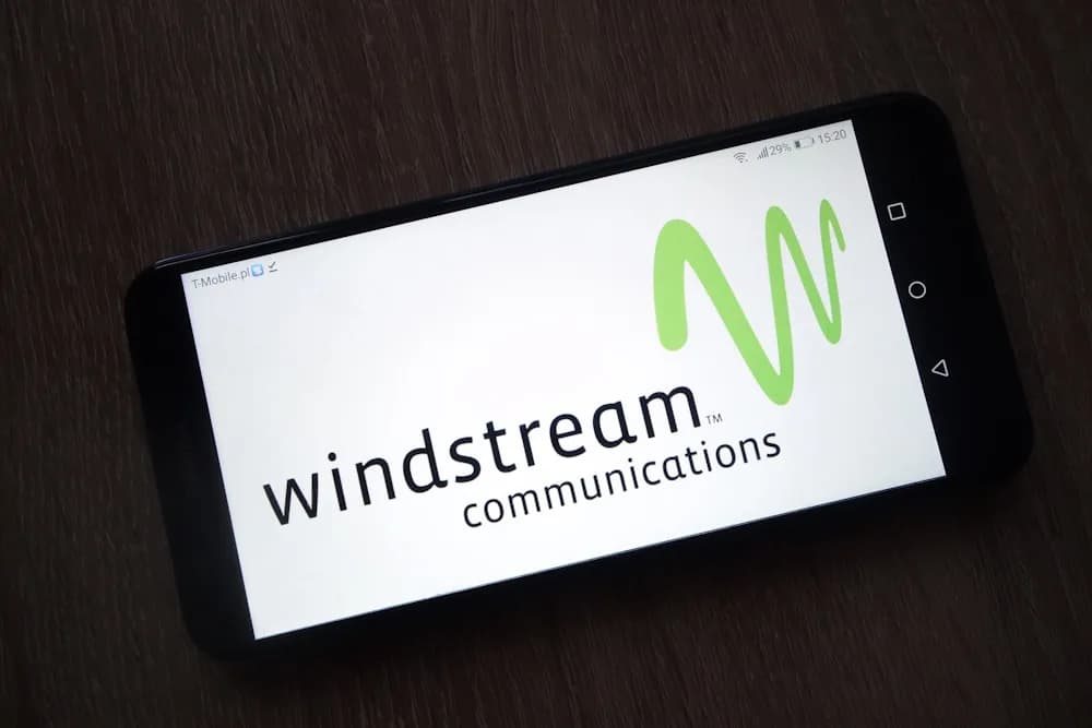 A phone on a dark wooden surface displaying the Windstream Communications logo